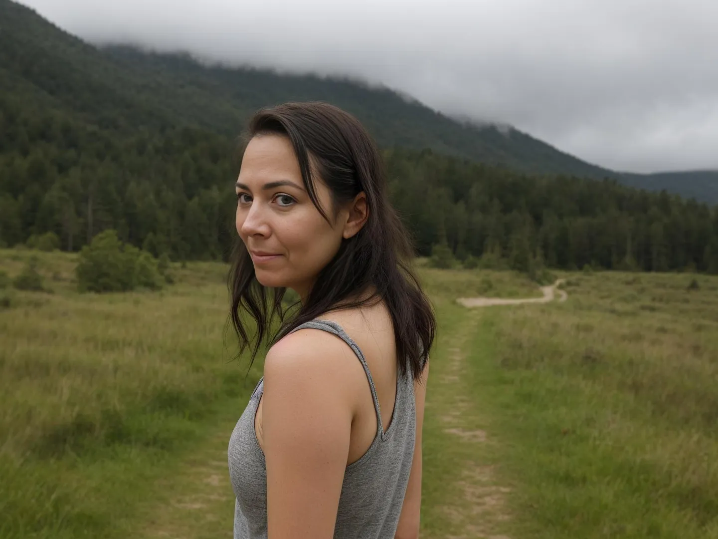 A woman with dark hair wearing a grey tank top standing on a grassy path in a mountainous landscape, AI generated image using stable diffusion.